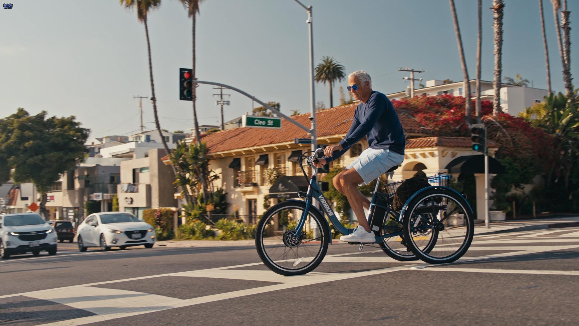 Man riding a bicycle on a city street with palm trees and buildings in the background