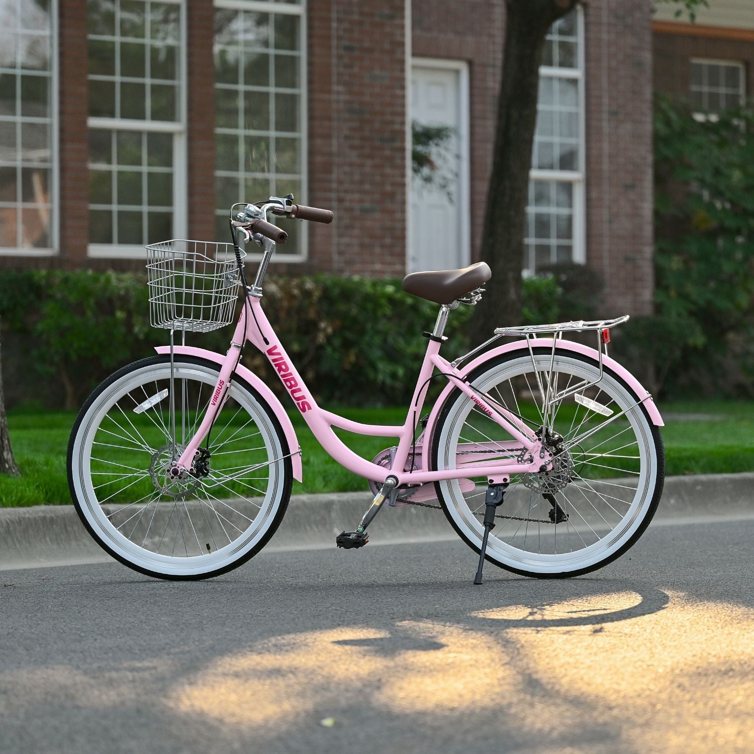 Pink bicycle with a basket parked on a street in front of a brick building.