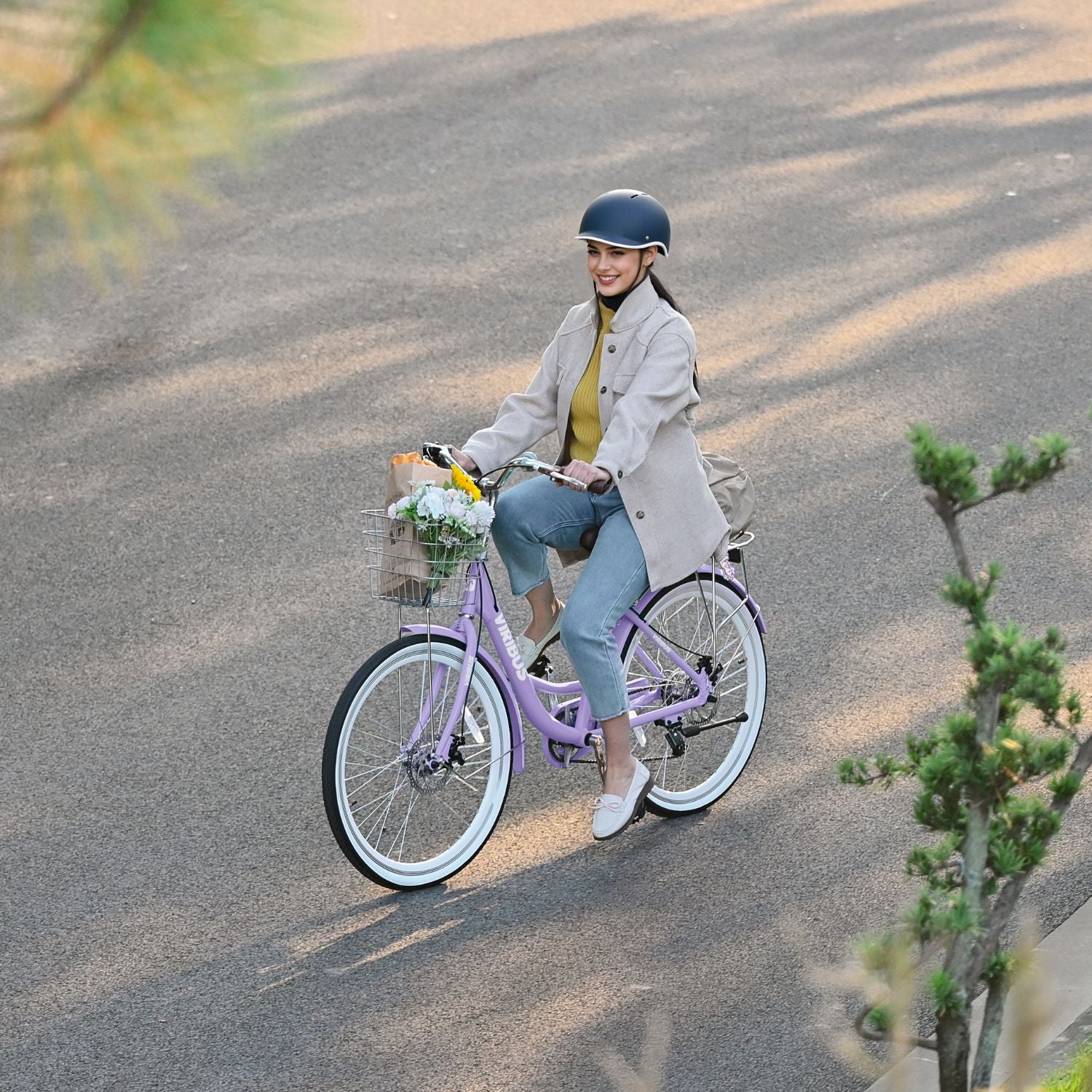 Woman riding a purple bicycle with a basket on a paved path